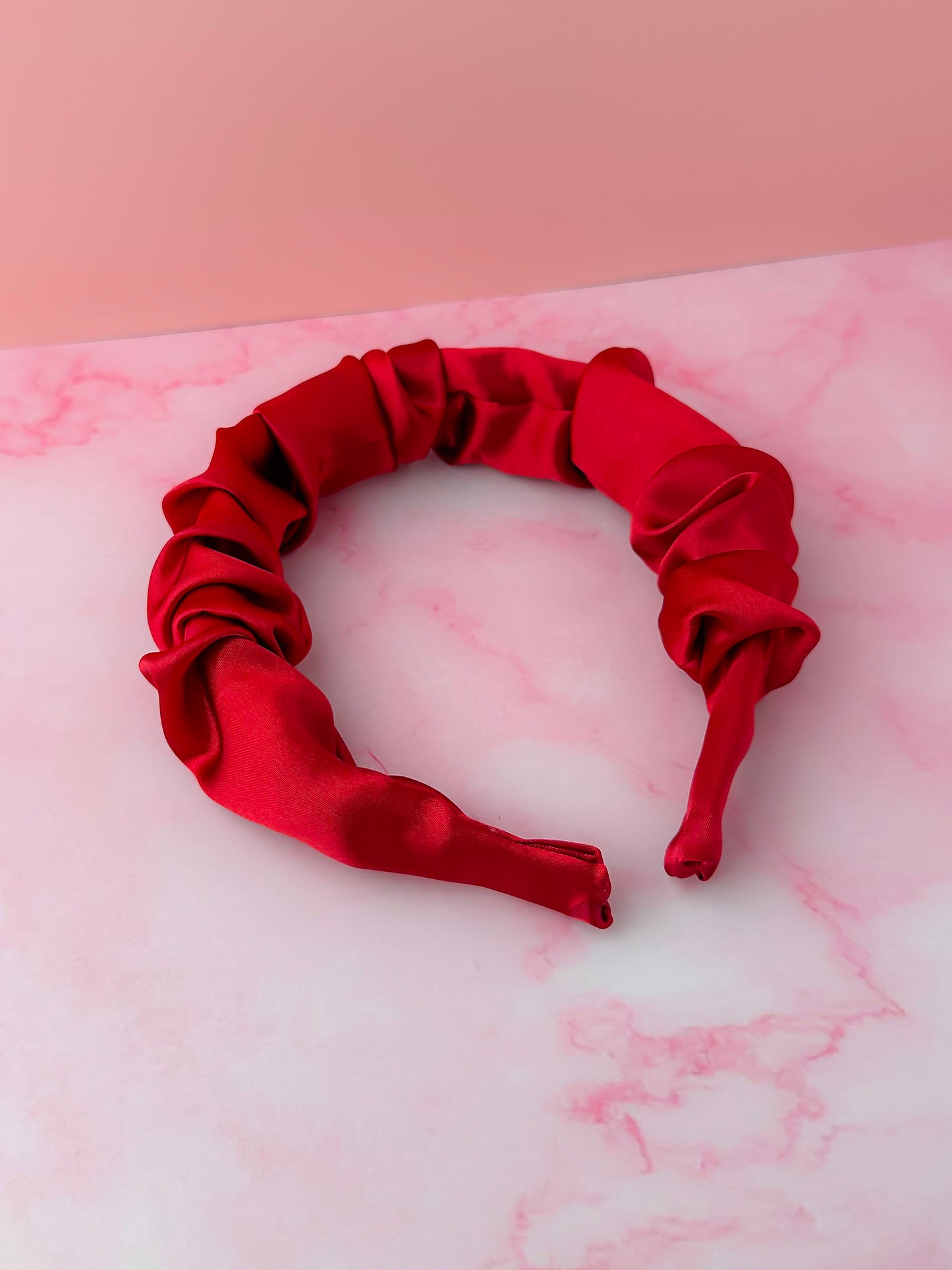 Red satin headband on a pink and white marble surface