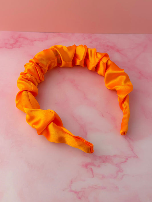 Orange satin headband on a pink marble surface