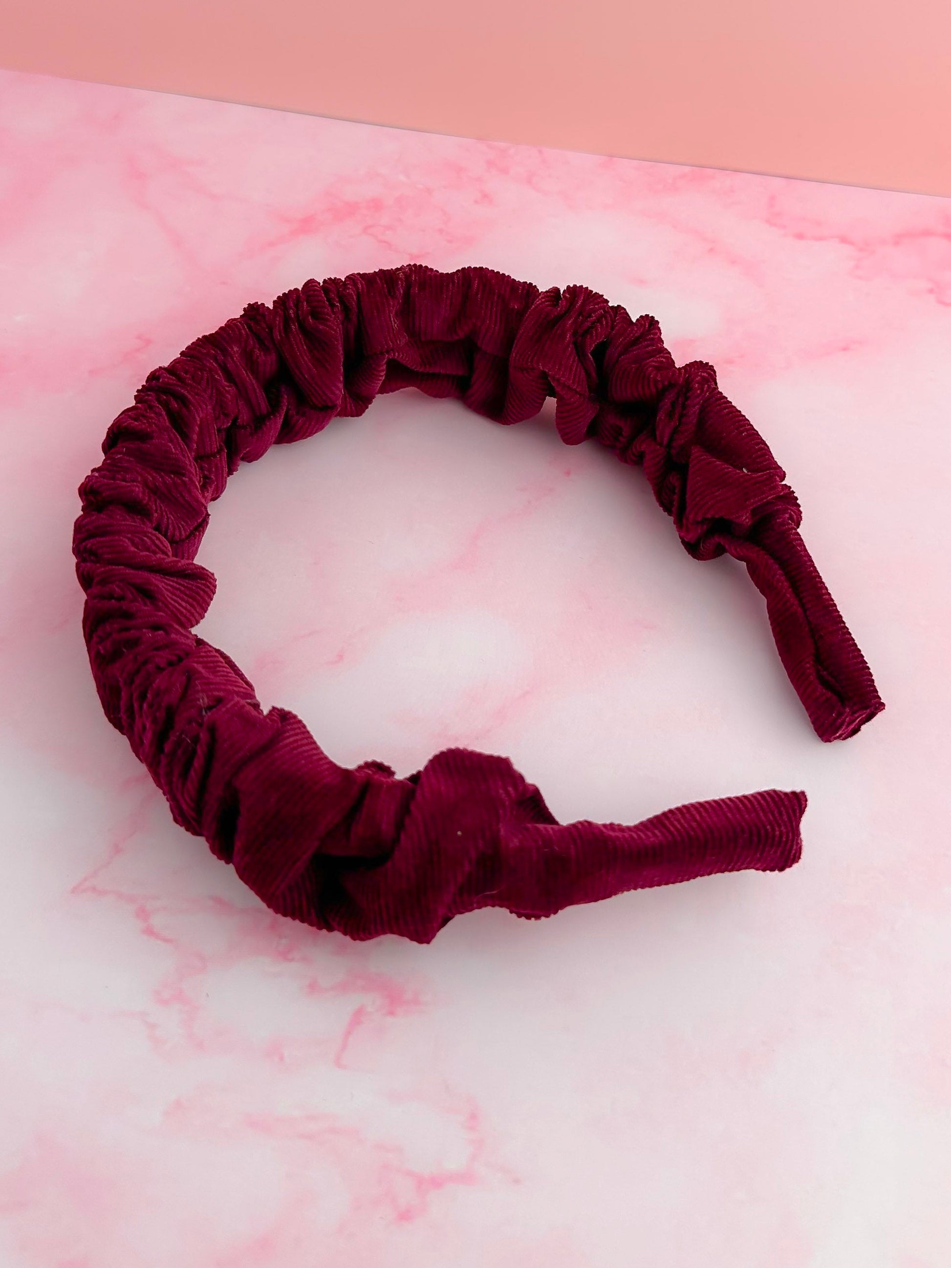 Burgundy velvet headband on a pink and white marble surface